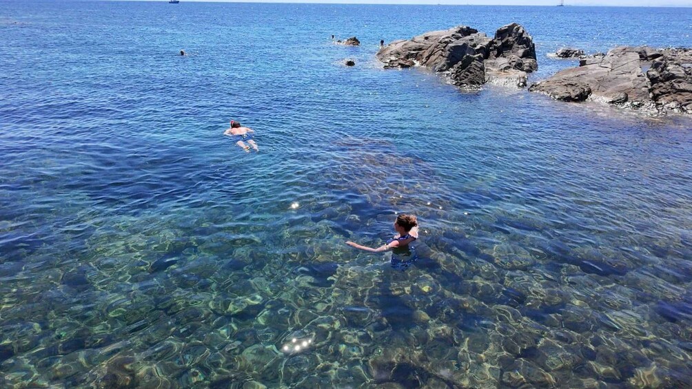 Two people swimming in clear blue water near rocky shores. 2