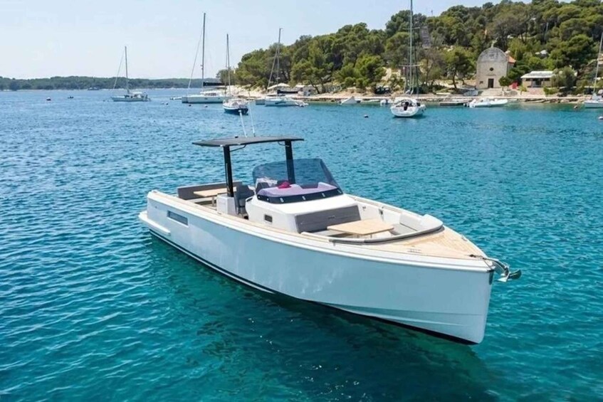 A white motorboat on clear blue water with a docked rowboat in the background and a building on a hill. 3