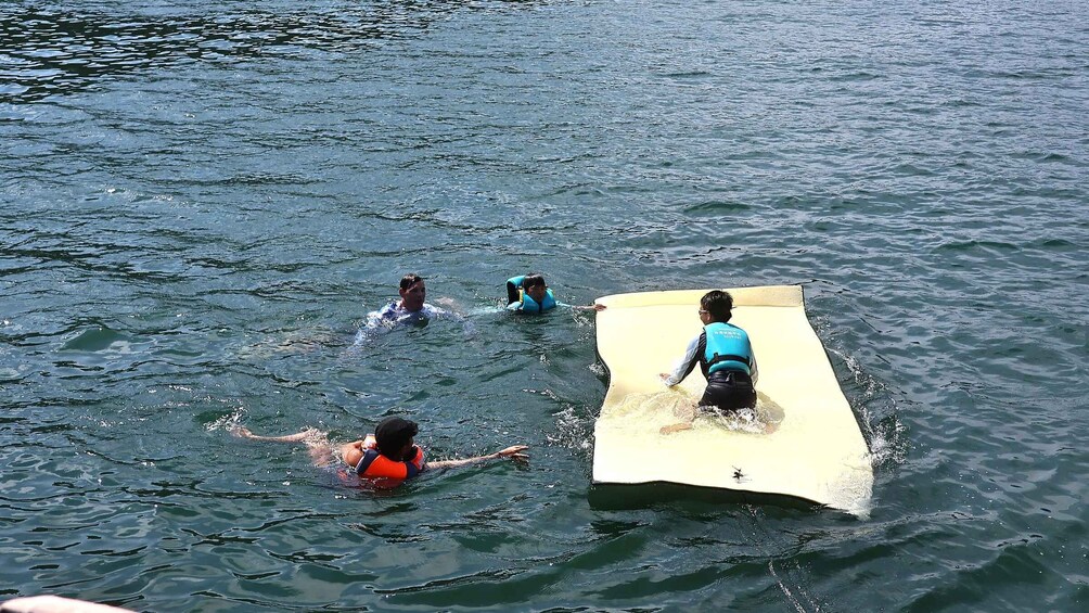 Three people in the water with a surfboard. 5