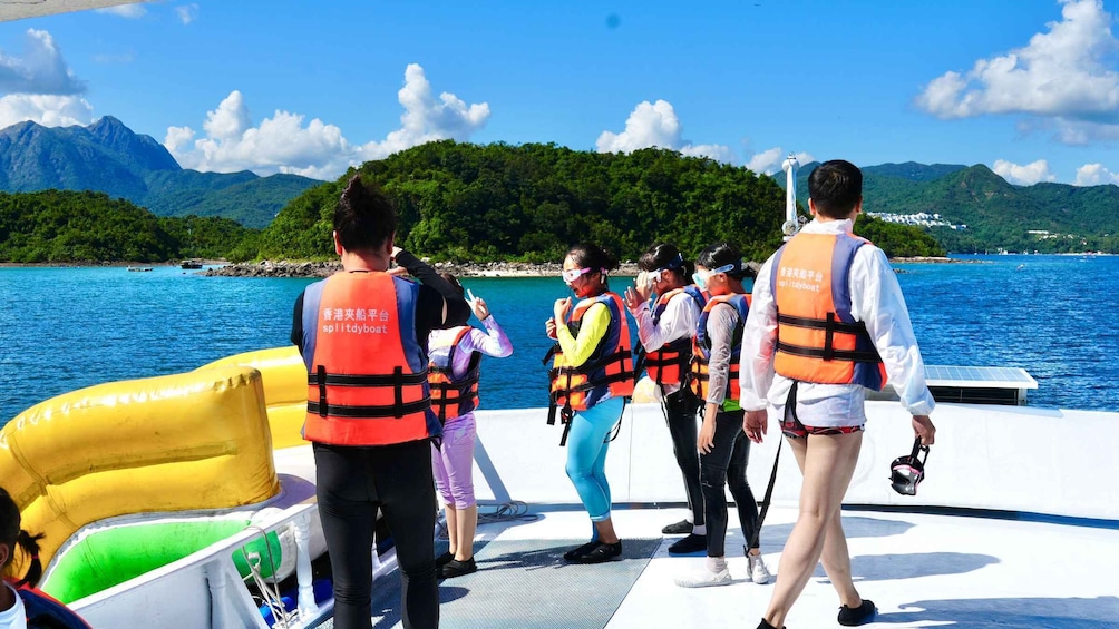 A group of people on a boat wearing life jackets, with a mountainous landscape and a clear blue sky in the background. 4