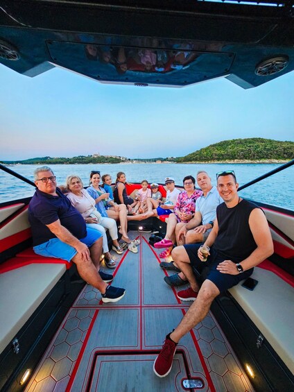 A group of people on a boat with a view of a green island and water. 1