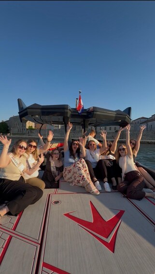 A group of people on a boat with a red arrow on the deck, a flag, and a historic building in the background. 2