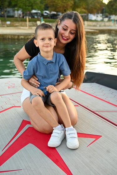 A woman and a child sitting on a boat with a water body in the background. 3