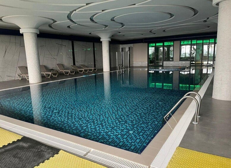 An indoor swimming pool with a blue tiled floor, white columns, and a yellow tactile path leading to the pool. 3