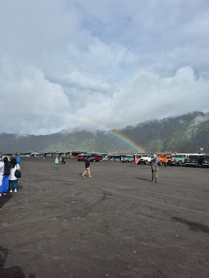 A parking lot with a rainbow, people, and vehicles. 3