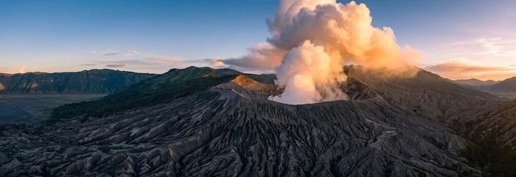 A volcanic landscape with a large plume of smoke or steam rising from the center. 5