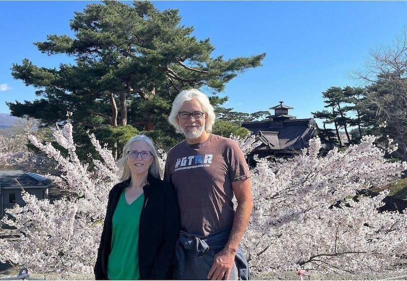 Two people standing in front of cherry blossoms with a traditional Japanese building in the background. 4