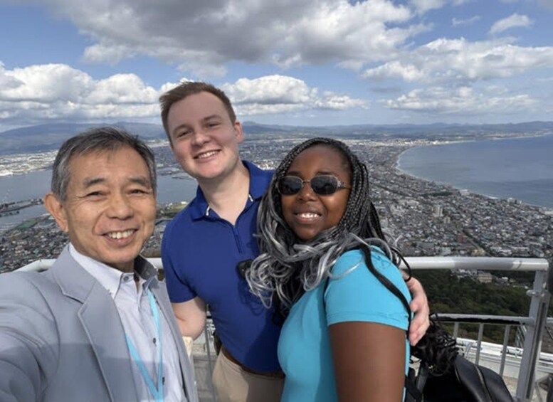 Three people taking a selfie with a cityscape and coastline in the background. 5