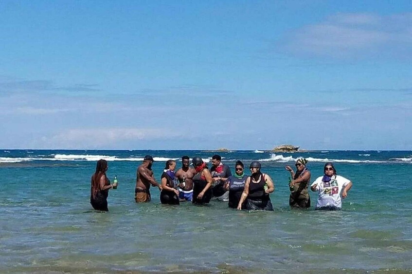A group of people standing in shallow water at the beach with the ocean in the background. 3