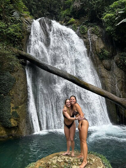 A waterfall with two people standing on a rock in front of it. 4