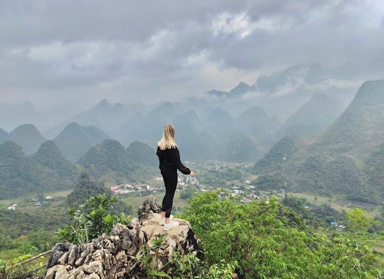 A person standing on a rocky outcrop overlooking a valley with mountains in the distance. 3