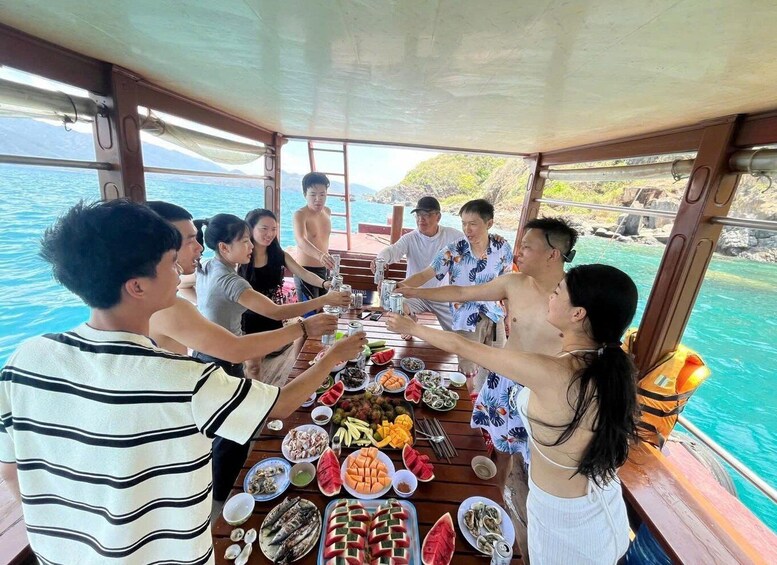 Un grupo de personas brindando con bebidas en un barco, con una mesa llena de comida y una vista panorámica del mar. 1