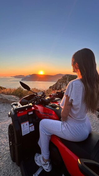 A person sitting on a red ATV with 'Force 625' written on it, overlooking a sunset over a body of water and rocky terrain. 1