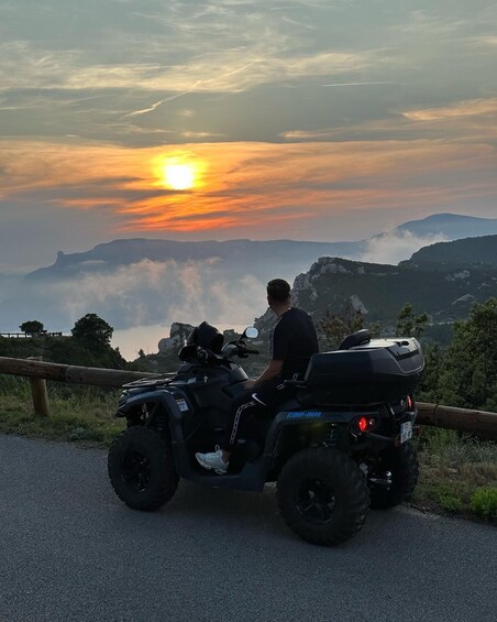 A person riding a black ATV on a road with a sunset in the background. 4