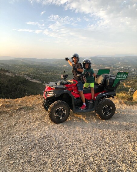 Two people on a red ATV with a green sign, overlooking a mountainous landscape. 5