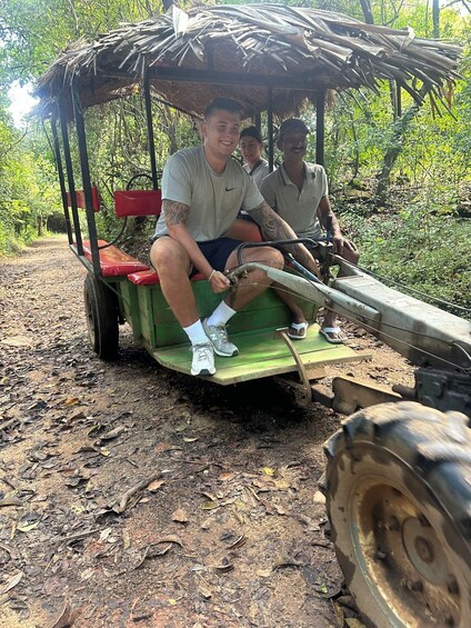 A man driving a green cart with a thatched roof through a forested area. 3