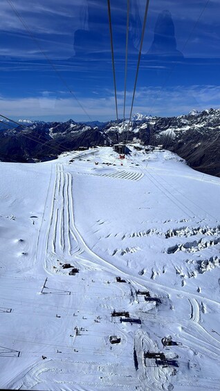 A snowy mountain slope with ski tracks, a ski lift, and a distant mountain peak. 2