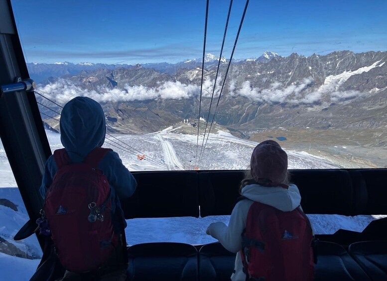 Two people in red jackets observing a snowy landscape with mountains and a clear sky. 3