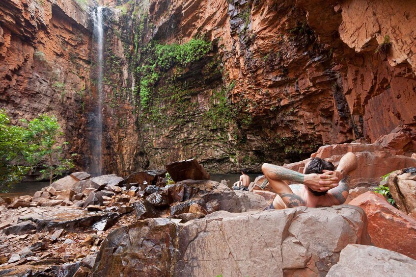 A waterfall in a rocky canyon with a person sitting on rocks. 4
