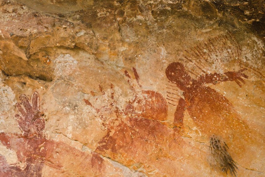 A cave wall with ancient rock paintings of human figures and animals. 3