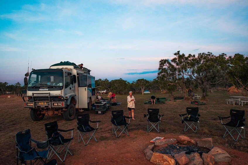 A camping site with a large Isuzu truck, several black camping chairs, a fire pit, and a picnic table. 1