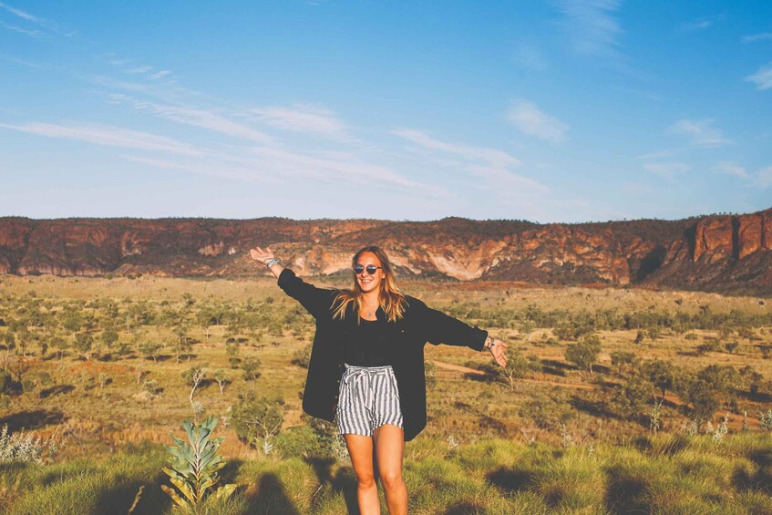 A person standing in a grassy field with a mountainous landscape in the background. 2