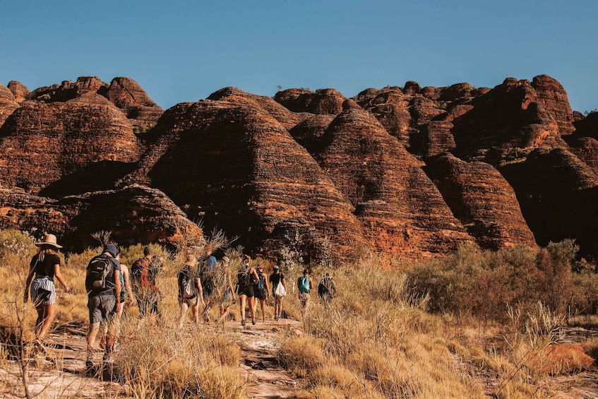 A group of hikers on a rocky trail with red rock formations in the background. 1