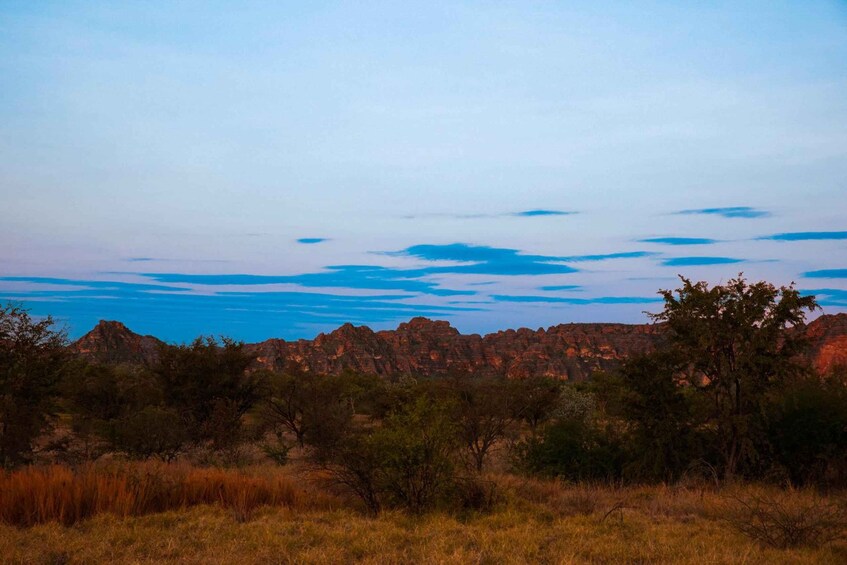 A landscape with red rock formations, green trees, and a clear sky. 5
