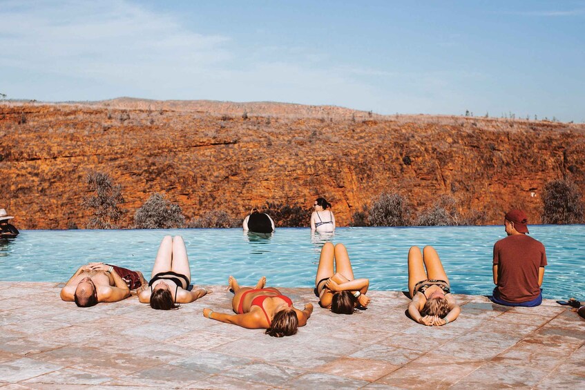 A group of people sunbathing by a pool with a rocky hillside in the background. 2