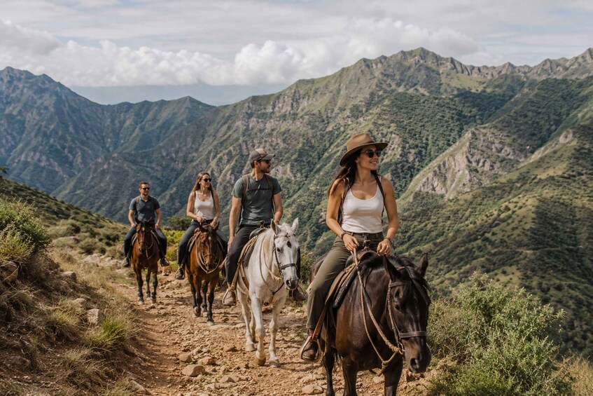 A group of people horseback riding on a mountain trail with green hills in the background. 3