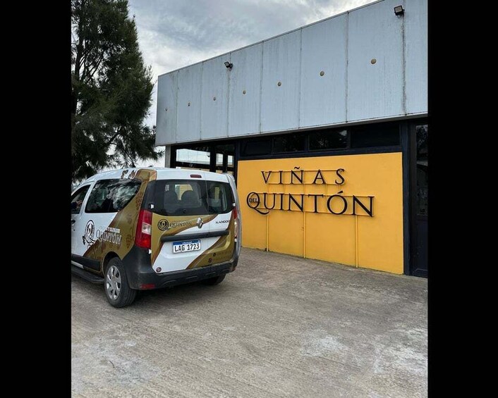 A white van parked in front of a building with a yellow wall and the text 'VINAS QUINTÓN' on it. 1