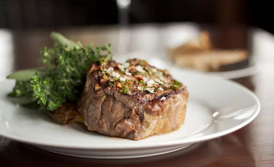 A steak with a garnish of herbs and vegetables on a white plate. 4