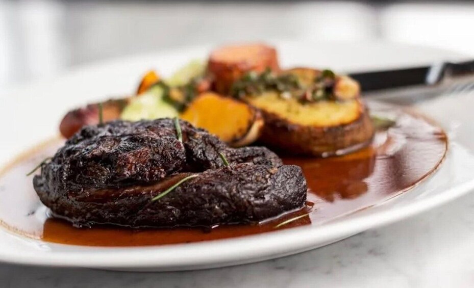 A plate of food with a darkly grilled meat, roasted vegetables, and a slice of bread. 1