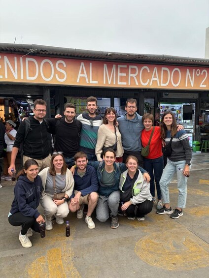 A group of people posing in front of a market stall with a sign reading 'NIDOS AL MERCADO N°2'. 4