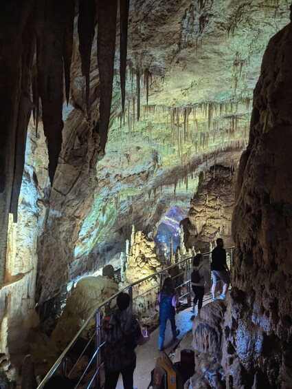 A cave with stalactites and stalagmites, people walking on a path, and a railing for safety. 2