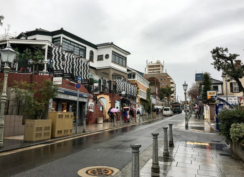 A wet city street with shops, a bus, and pedestrians under an overcast sky. 2