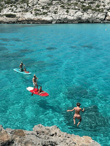 People paddleboarding in clear turquoise water with rocky cliffs in the background. 3