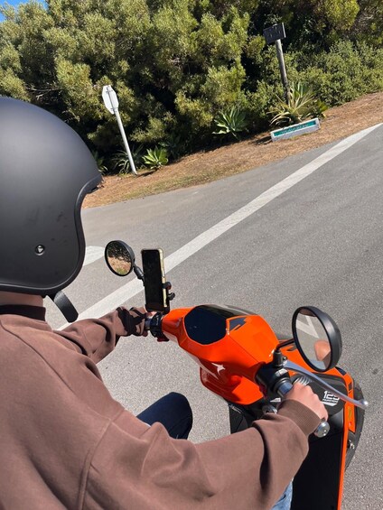 A person riding a red scooter on a road with a green sign in the background. 2