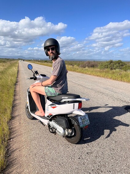 A person riding a white scooter on a gravel road with grass on the sides. 5