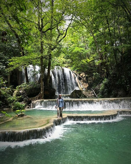 A waterfall cascading over terraced steps in a forested area with a person standing on the steps. 1