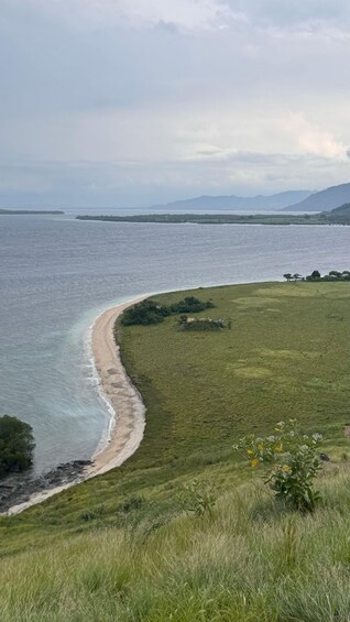 A coastal landscape with a sandy beach, grassy fields, and distant mountains under a cloudy sky. 2
