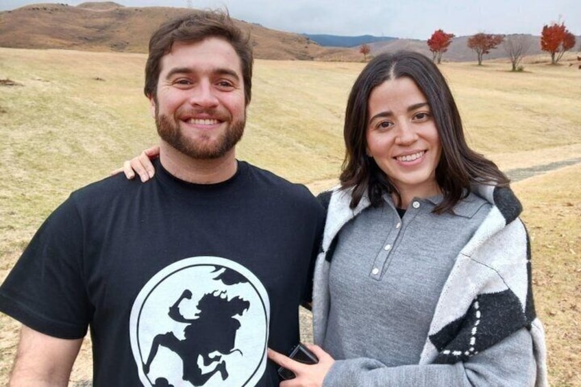 Two people standing in a grassy field with hills in the background. 4