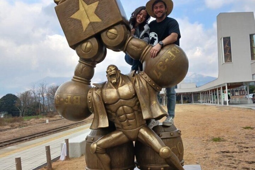 A large golden robot sculpture with a star on its chest, a person sitting on its shoulder, and a building in the background. 5