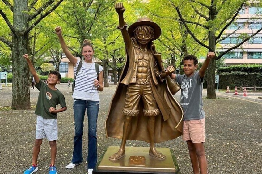 A bronze statue of a character with raised arms, surrounded by trees and a paved area. 2