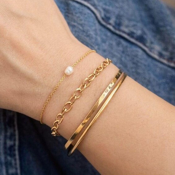 A wrist with three gold bracelets, one with a pearl. 1