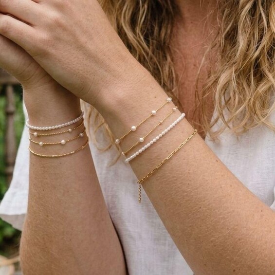 A person wearing multiple gold bracelets with pearls. 3