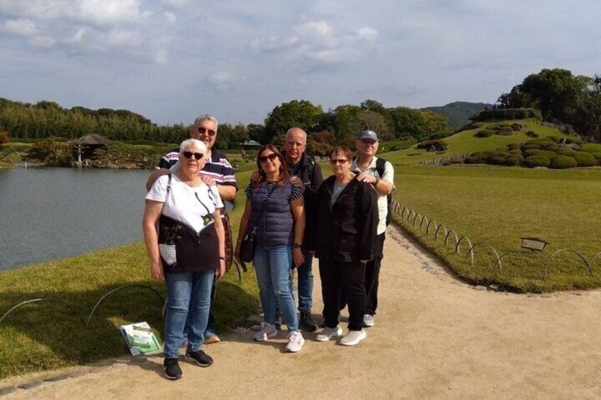 A group of people standing on a path near a lake with a hilly landscape in the background. 5