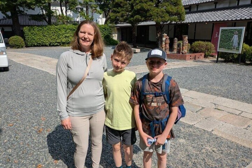 Three people standing in a courtyard with stone flooring and traditional Japanese architecture in the background. 4