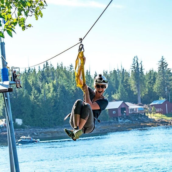 A person zip-lining over a body of water with a forest and buildings in the background. 1