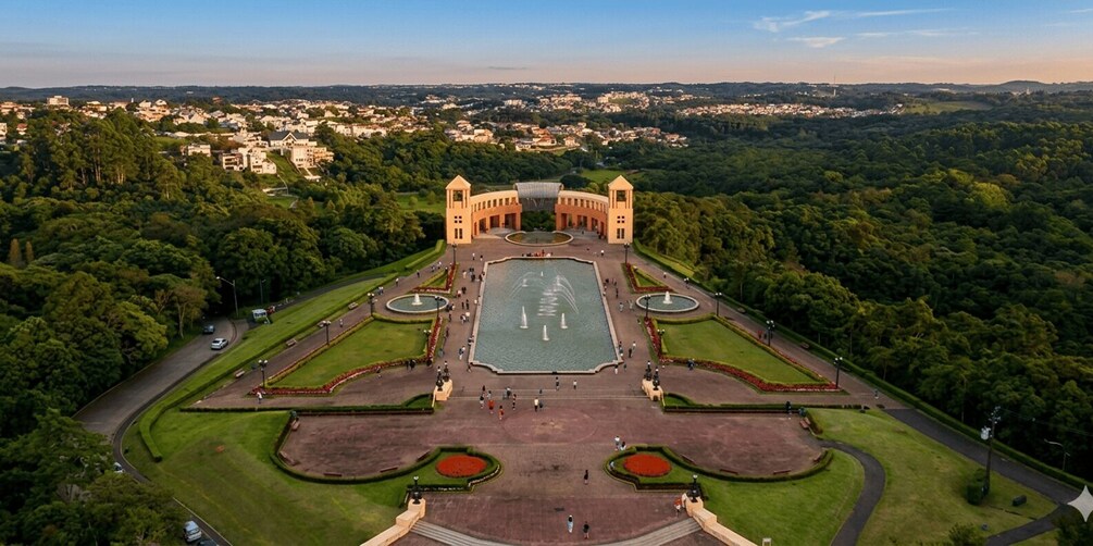 A large, symmetrical garden with fountains, surrounded by lush greenery and a distant town. 2